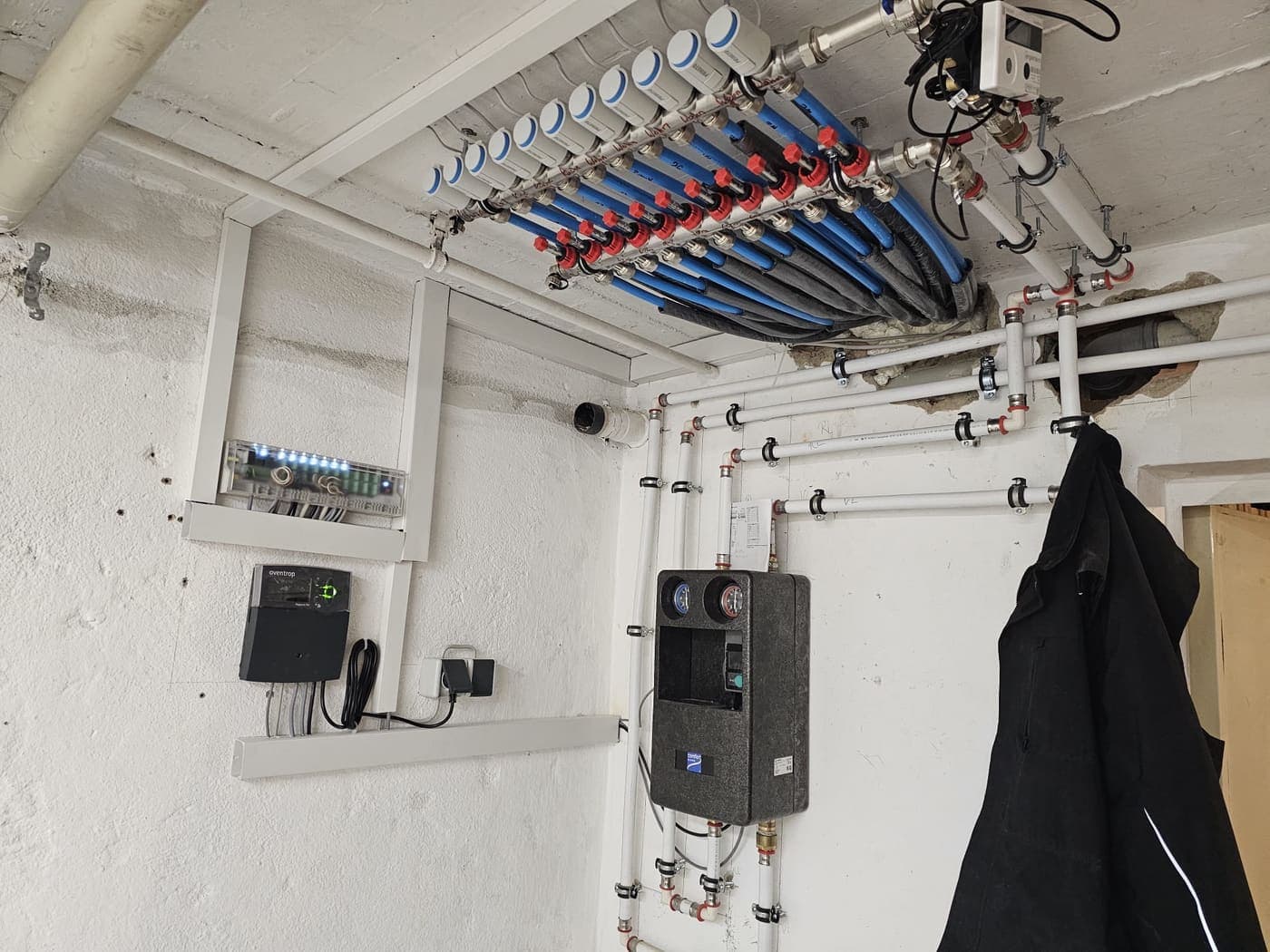 Technikraum: Deckenverteilung mit Absperrventilen und Zähler, an der Wand die Übergabestation und die Regelung.
