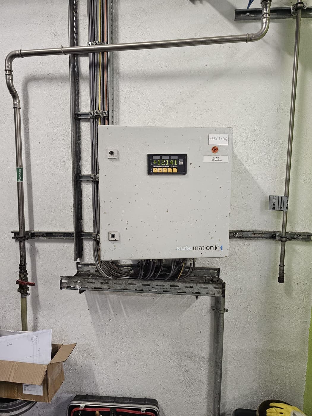 Industrieller Steuerschrank mit digitaler Gewichtsanzeige, daneben die Rohrleitungen für Wasser und Druckluft.
